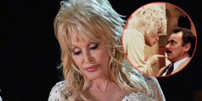 A woman with blonde hair and wearing a sparkly white outfit looks down thoughtfully. In the top right corner, there's an inset image of music legend Dolly Parton in white, pointing at a man in a suit.