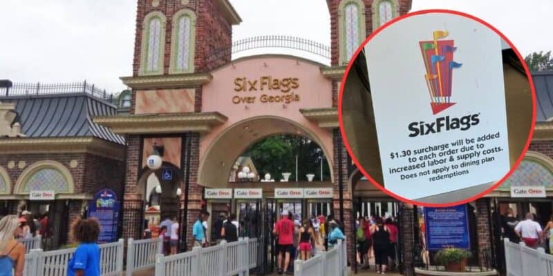 Entrance of Six Flags Over Georgia theme park with a sign in the foreground noting a $1.30 surcharge for orders due to increased labor and supply costs. People are visible near the gates.