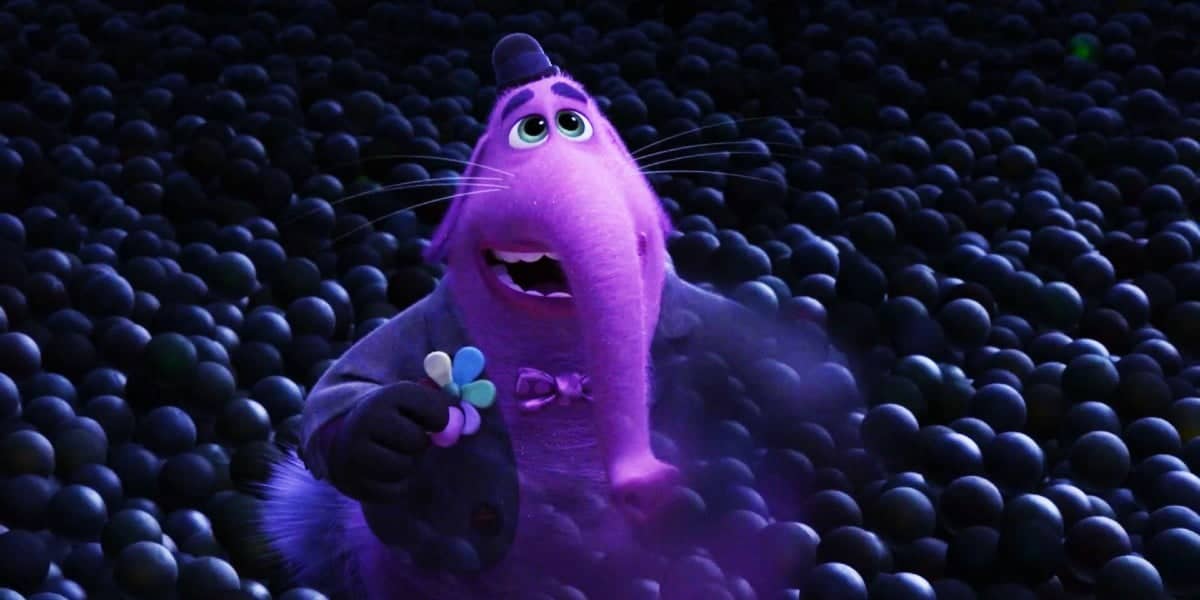 A purple, animated character with large eyes and shaggy fur, holding a microphone in one hand and three colorful candies in the other, surrounded by a crowd of black spheres.