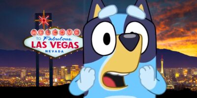 An animated blue dog character, Bluey, stands in front of the illuminated "Welcome to Fabulous Las Vegas Nevada" sign at dusk. The vibrant Las Vegas skyline brightens the darkening sky. Bluey looks surprised or shocked, as if he's just been called a bad dog in the bustling Vegas night.