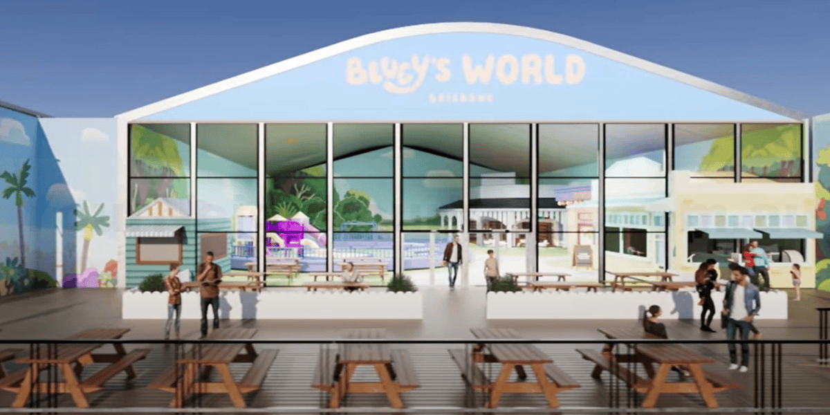 Illustration of the entrance to "Bluey's World Brisane," showing a vibrant, family-oriented attraction. The facade has a large glass windows and cheerful murals of beach scenes, patrons are seen entering and gathering at picnic tables outside.