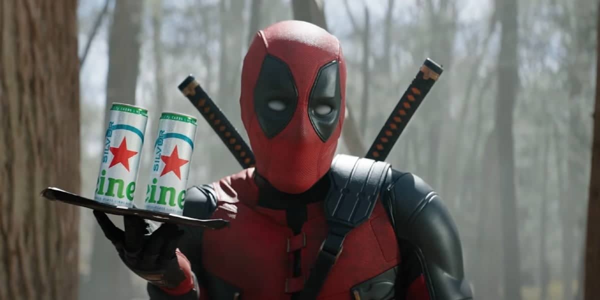 A person wearing a red and black costume with a mask, holding a tray with two cans. The setting appears to be a forest with misty surroundings. The costume includes a belt, body armor, and two swords on the back.
