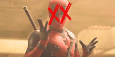 A person in a red and black Deadpool costume with crossed-out eyes gestures with their hands, standing in a foggy environment.