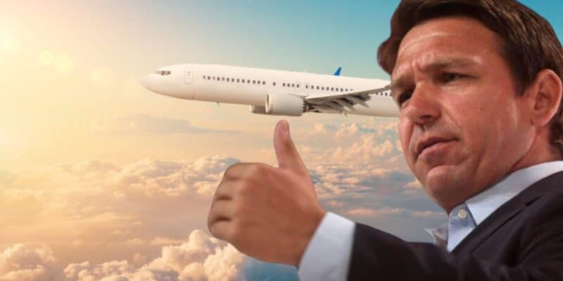 A man in a suit gives a thumbs-up gesture with an expression of approval. In the background, an airplane is flying through a sky filled with clouds, illuminated by the sun.