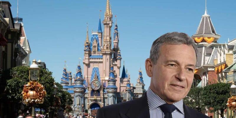 Bob Iger with a serious expression, dressed in a suit, superimposed on an image of a bustling Disneyland Main Street with a view of the decorated castle in the background.