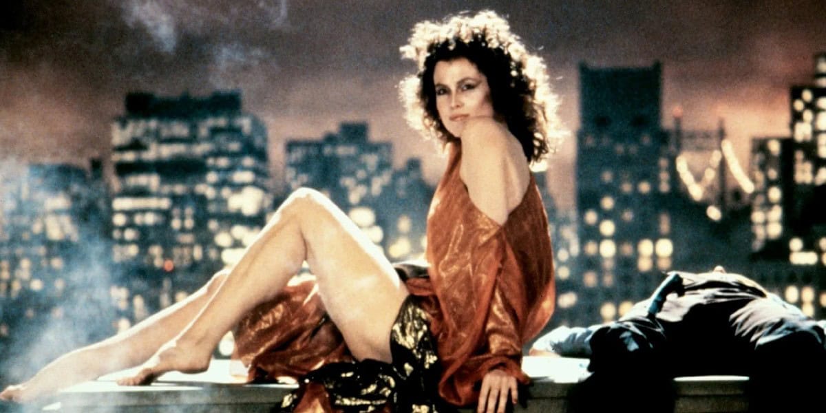 A woman in a shiny golden dress sits on a rooftop at twilight, with a dramatic cityscape in the background. Her relaxed pose and thoughtful expression add a serene vibe to the urban setting.