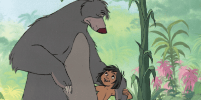 An animated scene featuring a friendly grey bear standing and holding hands with a smiling young boy with dark hair in a jungle setting. The background includes green foliage and colorful plants. The boy gazes up at the bear with a joyful expression.