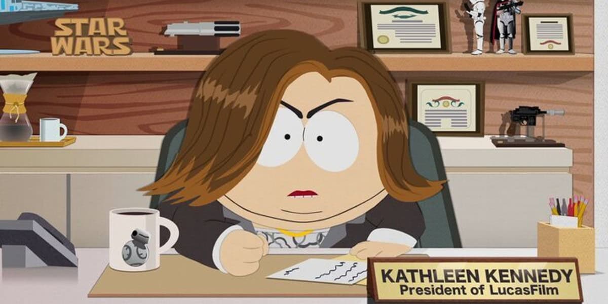A cartoon character with brown hair and a stern expression sits at a desk with a nameplate reading "Kathleen Kennedy, President of LucasFilm." The desk has various items including papers, a coffee maker, a mug, and Star Wars memorabilia in the background.