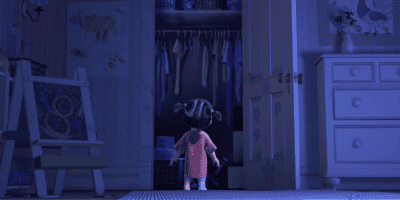 A young girl in a pink nightgown stands at the open door of a dimly lit closet in her bedroom, which is decorated with drawings and a white dresser inspired by Monsters Inc.