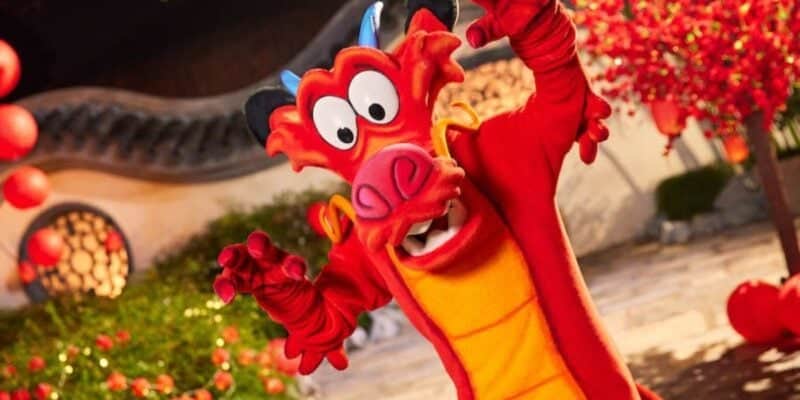 A costumed character of Mushu, a red dragon with a yellow belly, from Disney's "Mulan," is posing energetically. The background features Chinese architectural elements and red lanterns, creating a festive atmosphere.