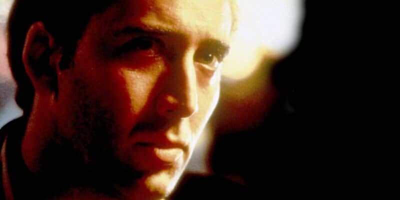Close-up of a man with a serious expression, lit by warm, golden light, casting shadows on his face, focusing on his eyes and the contours of his face.