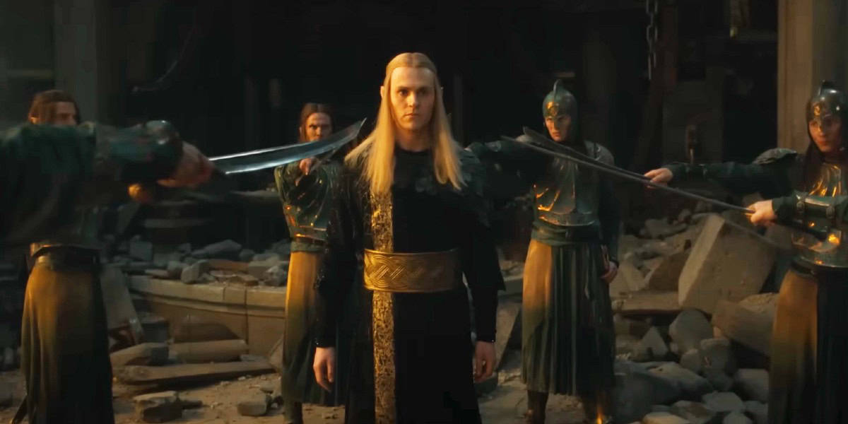 A person with long blond hair stands in the center, looking determined, while surrounded by four armored individuals with swords pointed at them. The background depicts a dimly-lit, rubble-filled setting, suggesting a tense and dramatic scene.