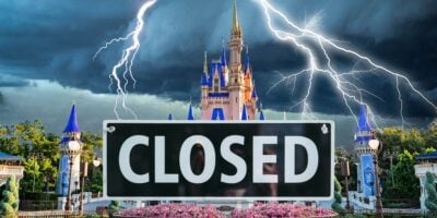 A Disney castle looms under a dark, stormy sky, with multiple lightning strikes piercing the heavens. In the foreground, a sign displaying "CLOSED" heightens the atmosphere of suspense and foreboding.
