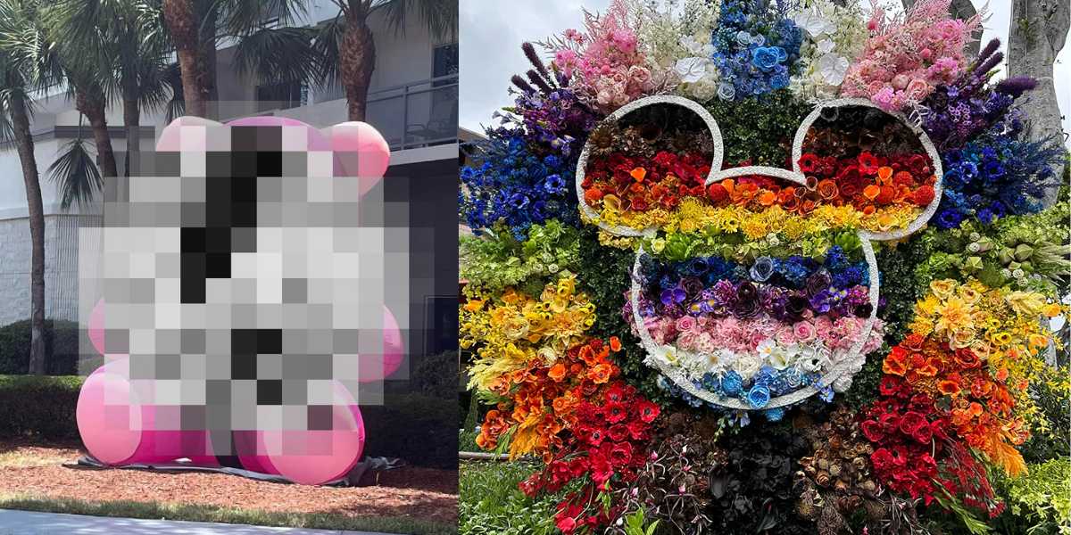 A large floral arrangement shaped like Mickey Mouse's head and ears adorns the entrance of the hotel. The vibrant, multicolored flowers are arranged in stunning rainbow patterns, echoing Pride decorations. Palm trees and a building are visible in the background, adding to the magical Walt Disney World atmosphere.