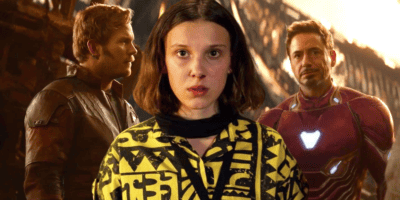 A young person wearing a brightly patterned yellow jacket stands in the foreground, looking ahead with a serious expression. Behind them are two individuals: one wearing a red and gold armored suit reminiscent of the Avengers on the right, and the other in a brown jacket on the left.