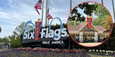 The image shows the entrance sign for Six Flags Great America, which features colorful flags and the park's logo. In the background are trees and American flags. The inset highlights the entrance gate, also displaying the park's logo. Flower beds line the foreground.