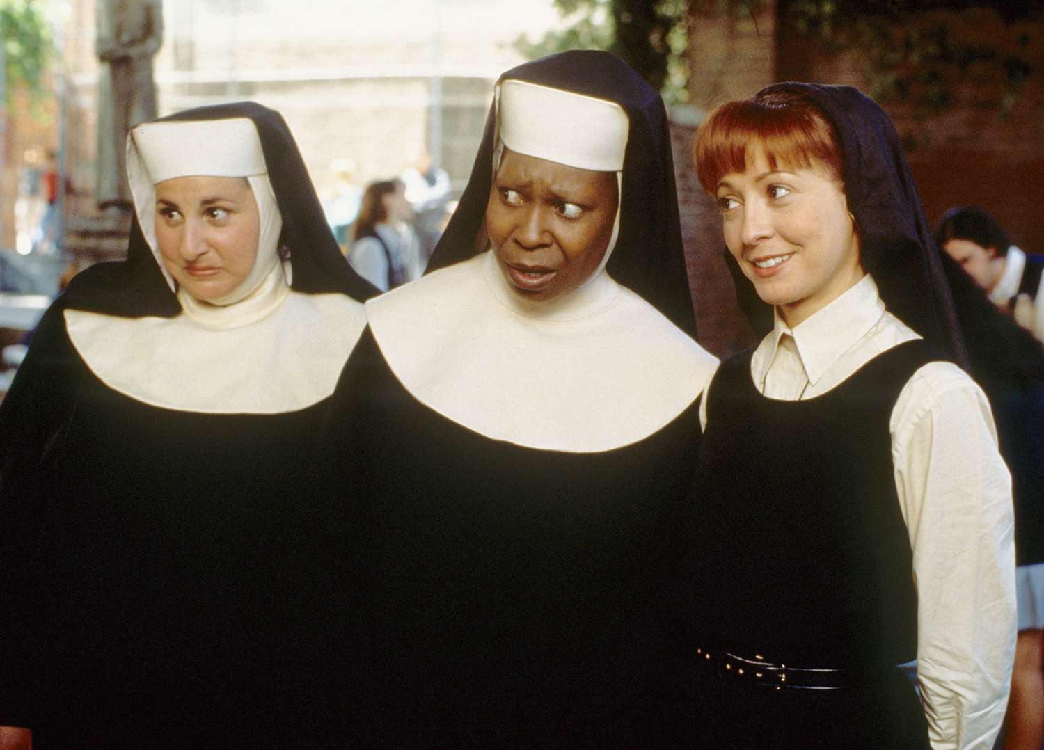 Three women dressed as nuns, reminiscent of "Sister Act," stand together. The woman in the middle, with a surprised expression, channels her inner Whoopi Goldberg while the others smile at her. They are outdoors with other people visible in the background.