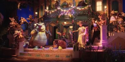 A vibrant scene featuring various colorful characters from Disney's "The Princess and the Frog" is set in front of a lively, decorated New Orleans-style building. The characters are in mid-performance, with musicians playing instruments and others dancing and singing, the finale of Tiana’s Bayou Adventure.