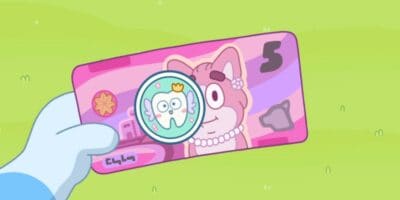 A simplified cartoon hand is holding a pink five-dollar bill featuring a smiling character, possibly Bluey, wearing a pearl necklace. The bill also includes a circular emblem with a cartoon tooth wearing a crown. The background is light green.