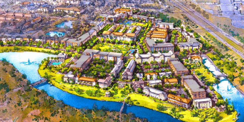 An aerial illustration of a planned urban development featuring multiple clusters of buildings arranged around green spaces and winding pathways. A river borders two sides of the development, with a bridge crossing over it. Surrounding areas include roads and additional structures. Disney World affordable housing project