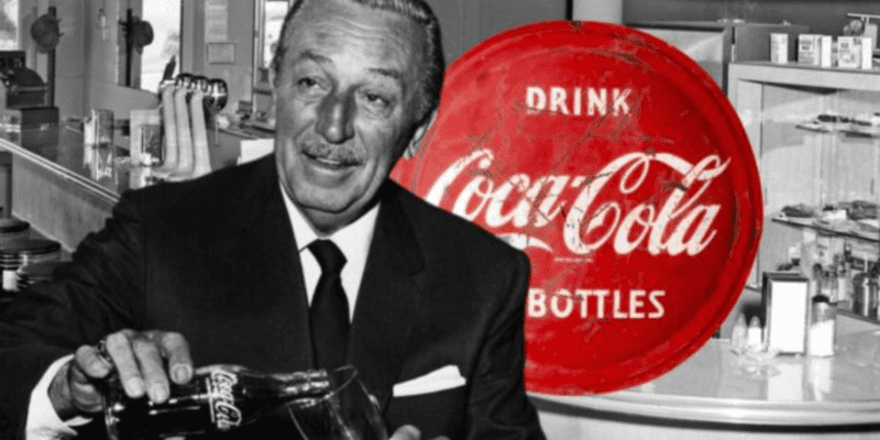 A black and white photo shows an older, smiling man in a suit and tie pouring a drink from a Coca-Cola bottle into a glass. Behind him is a large vintage red Coca-Cola sign with the slogan "Drink Coca-Cola in Bottles" in white font. The background features a diner setting, reminiscent of classic Disneyland charm.