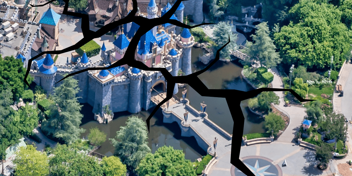 An aerial view of a Disney Park with a large castle at its center. The image is overlaid with a digitally added effect of large cracks spreading across the scene, as if an earthquake had rattled the ground. Lush greenery and water features surround the castle.