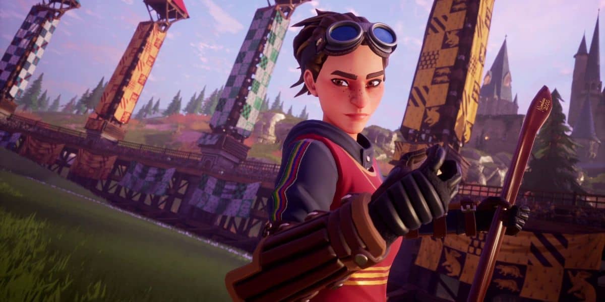 A character with short hair and wearing goggles, a dark red jersey, and gloves stands confidently with a clenched fist on a Quidditch field. The background features stadium towers adorned with colorful pennants and a castle in the distance, reminiscent of the magical world of Harry Potter by JK Rowling.