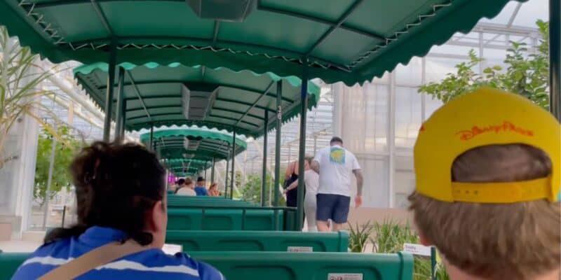 A group of people ride in green, covered tram cars through a greenhouse on Living with the Land.