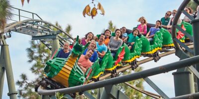 A group of people ride a colorful, dragon-themed roller coaster with green and yellow tracks at the theme park.