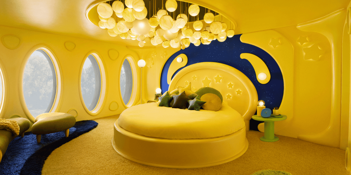 A vibrant bedroom features a round yellow bed with a crescent moon and star headboard, circular windows, and a unique chandelier of spherical lights. The room is predominantly yellow with playful decor elements, creating a whimsical, space-themed atmosphere.
