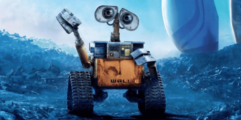 A rusty, yellow robot with large binocular-like eyes, named WALL-E, waves with one of its mechanical arms. The robot stands on rugged terrain with scattered debris, with a backdrop of a cloudy blue sky and large futuristic structures.