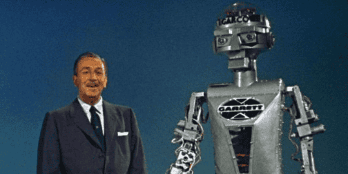 A man in a suit stands beside a vintage chrome robot with a retro design. The robot has a rectangular torso, and its head features lights and mechanical parts. The background is a solid blue color.