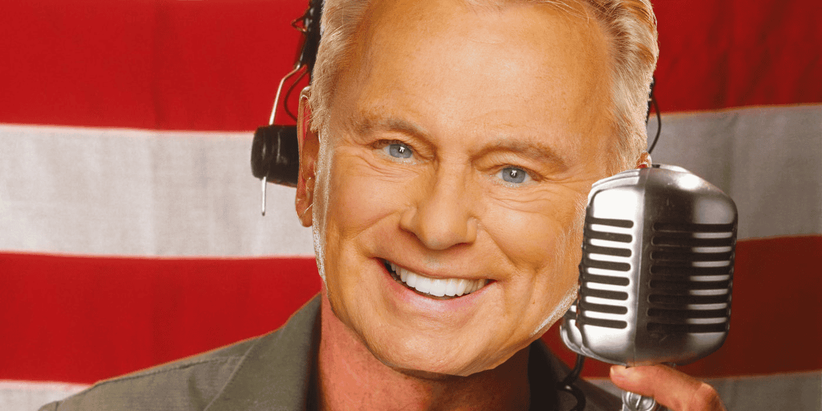 A cheerful person with short, light-colored hair is smiling brightly while holding an old-fashioned microphone close to their face. They are wearing a headset and are in front of a backdrop featuring red and white stripes, entertaining millions of fans.