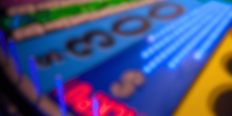 Abstract blurry image featuring vivid colors, primarily blues, greens, and reds. The colors and shapes are out of focus, creating a sense of motion and abstraction, with some areas appearing to have neon light effects reminiscent of a Wheel of Fortune backdrop. Specific details and objects are indistinguishable.