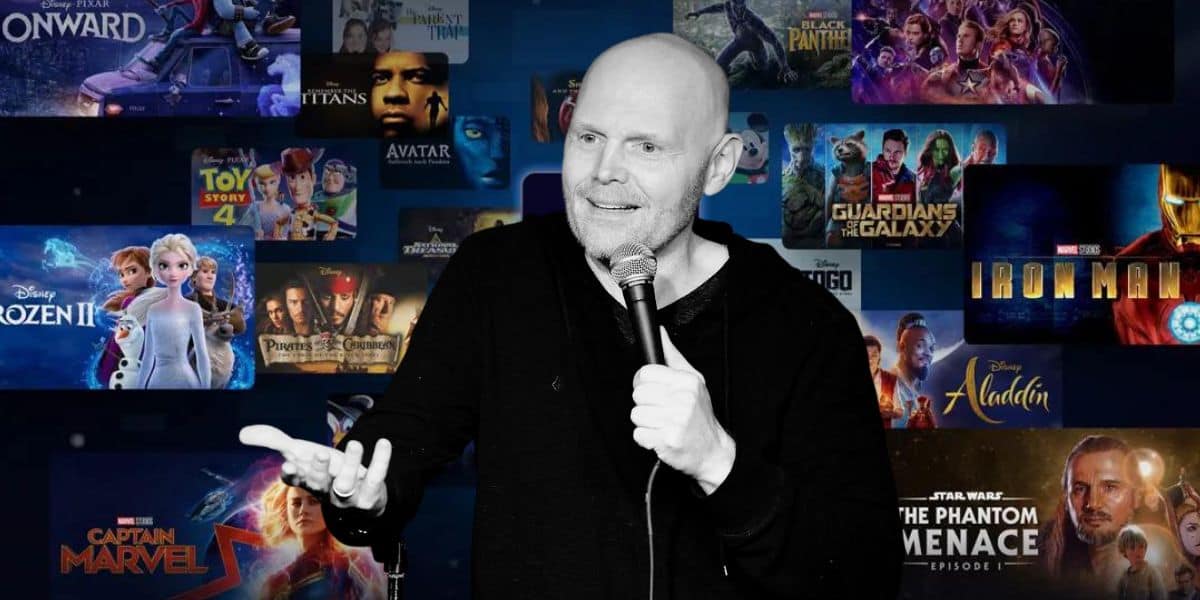 Comedian performs stand-up holding a microphone, with a collage of popular movie posters including "Frozen II", "Avatar", "Guardians of the Galaxy", "Iron Man", "Toy Story 4", and "Captain Marvel" in the background, teasing a new project potentially airing on Disney+ alongside hits like The Mandalorian.