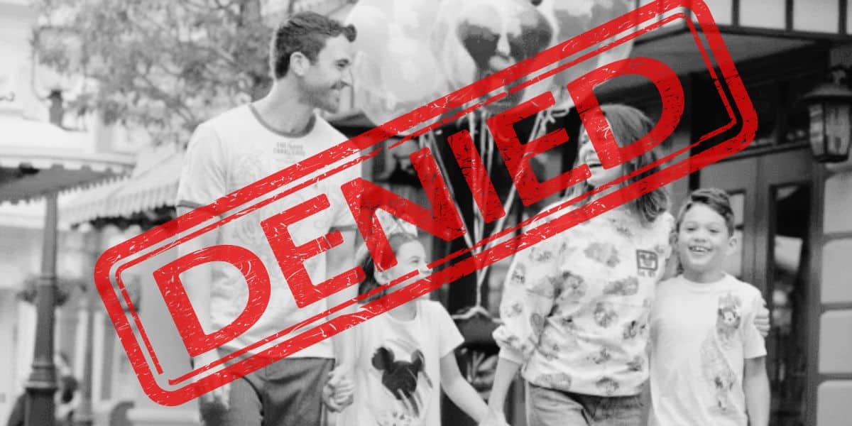 Black and white photo of a smiling family walking outdoors, reminiscent of a joyful day at Disney World. They consist of two adults and two children, holding balloons. A large red "DENIED" stamp overlays the image.