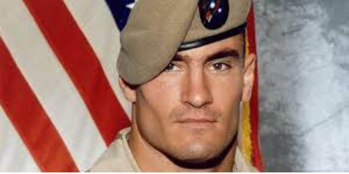 A person wearing a military uniform and a beret stands in front of an American flag. With a serious expression and short hair visible under the beret, the individual faces the camera, reminiscent of those honored with the Pat Tillman Award.