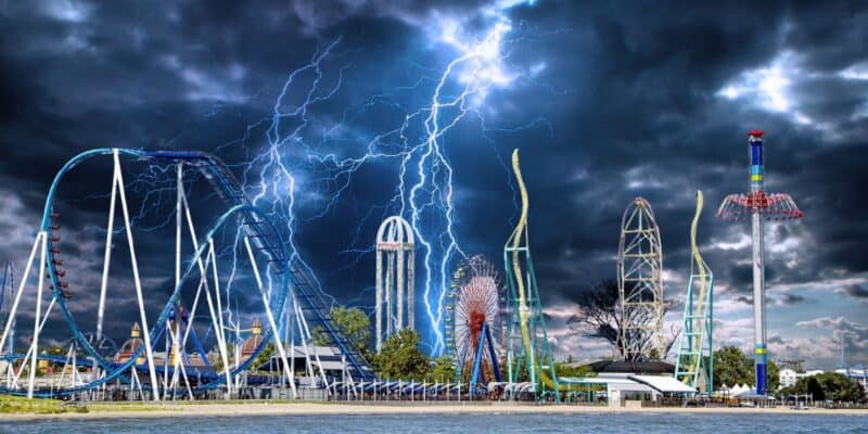 A dramatic scene unfolds at a theme park with roller coasters and rides set against a dark, stormy sky. Lightning bolts strike, illuminating the ominous clouds of what appears to be a Category 5 superstorm. The park is empty, with the thrill rides standing tall amidst the tempest.