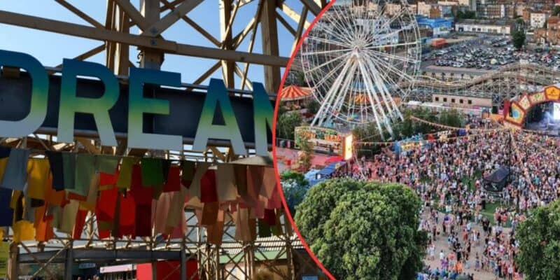 A festival scene with a Ferris wheel and a large crowd of people enjoying the event. Colorful flags hang under a structure with the word "DREAM" spelled out, reminiscent of a bustling theme park. The backdrop includes various festival booths and a parking area filled with cars.