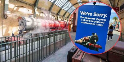 A red steam train, resembling the Hogwarts Express from Harry Potter, is stationed on tracks inside a covered platform. A nearby sign reads, "We're Sorry. The Hogwarts Express is closed for planned maintenance today." People walk in the background.