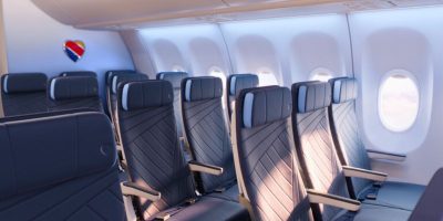 An empty row of economy seats on a brightly lit airplane from a popular airline, featuring dark blue leather upholstery. There are five windows visible along the side of the cabin, each providing a soft light. The airline's logo is displayed on the wall near the ceiling.