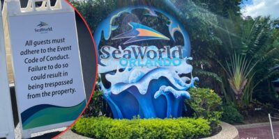 A bright sign at SeaWorld Orlando featuring a large logo of a wave and a tail fin, surrounded by greenery. Inset shows a notice stating all guests must adhere to the Event Code of Conduct or risk being trespassed from the property.