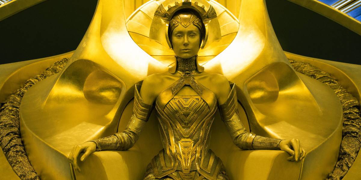 A futuristic warrior queen sits regally on a grand, ornately decorated golden throne. She wears intricate gold armor and a headpiece, and her expression is calm and stern. The throne and surroundings are lavishly designed with detailed metallic patterns.
