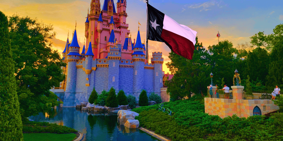 A majestic, fairy-tale castle with tall spires stands prominently against a vibrant sunset sky. A black, white, and red flag featuring a star flutters in the foreground, reminiscent of the Lone Star State. The scene is surrounded by lush greenery and a serene moat, enchanting all guests who wander by.
