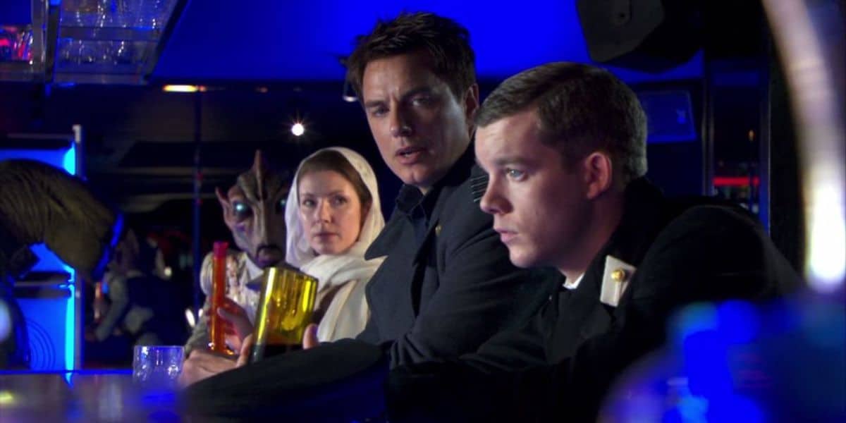 Three people are sitting at a bar in a room lit by blue lights. The first person holds a yellow glass, the second wears a white headscarf and looks surprised, resembling someone who just got new leads on a mystery, while the third person looks down with a serious expression. Another patron is seated in the background.