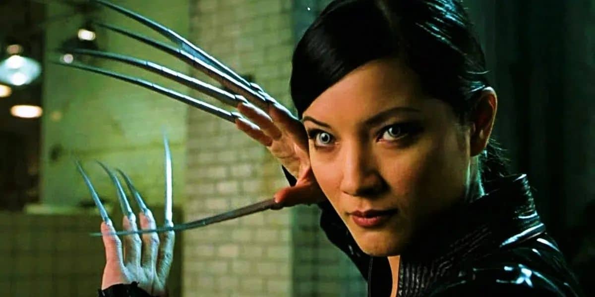 A woman with sleek black hair is seen in a dramatic pose, showing off long, metallic claws extending from her fingers, reminiscent of Wolverine. She has a determined expression and is wearing a black outfit. The background is a dimly lit industrial setting.