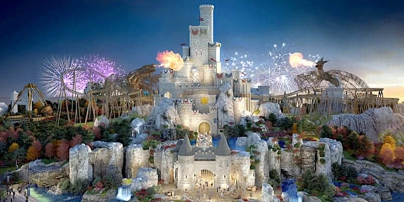 A grand castle with multiple towers stands illuminated against a twilight sky in what feels like a UK-themed Disneyland. Surrounding the castle are amusement park rides, colorful trees, and bursts of fireworks. Flamethrowers create spectacular flames, adding a magical feel to the theme park scene.