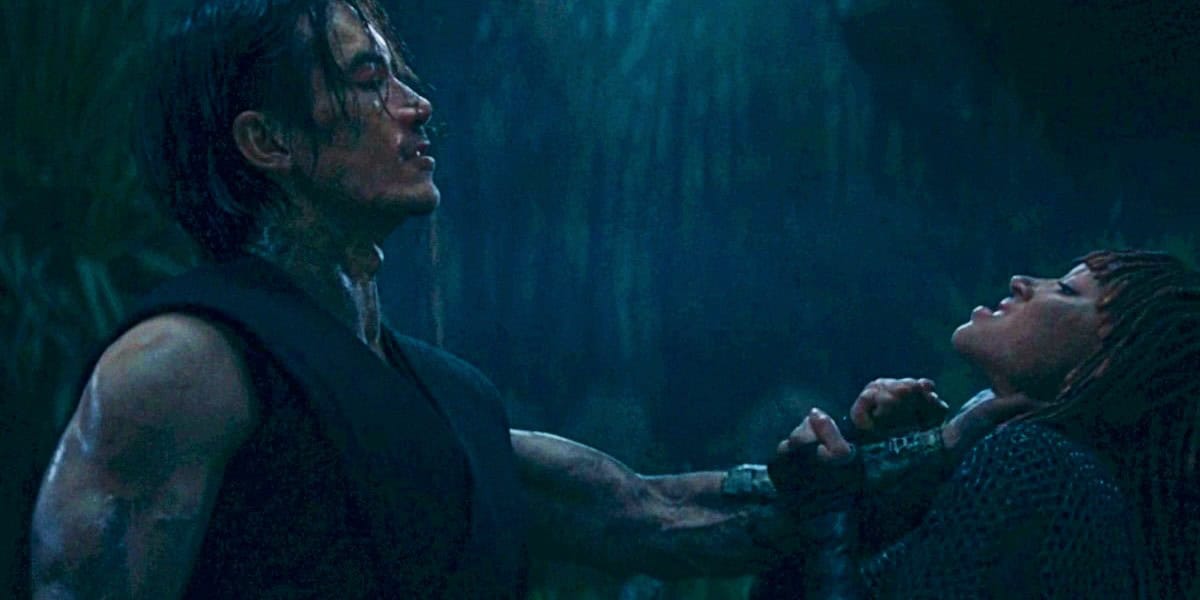 A person with long, wet hair, and tattoos on their arm, is holding their arm out with an intense expression, gripping another person's throat. The scene is dark, with dim lighting and a dense, jungle-like background. The second person appears to be struggling.