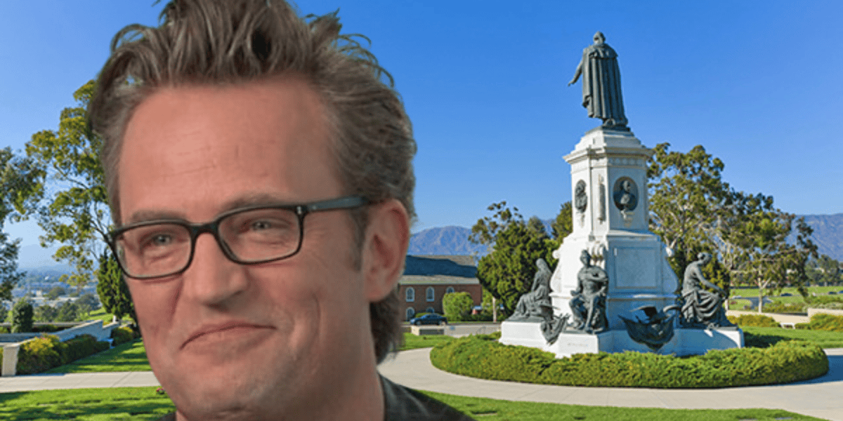 A man with glasses and tousled hair is smiling in the foreground of the image. Behind him is a large monument with statues, set in a park with green lawns and trees. A clear blue sky and mountains are visible in the background, reminiscent of picturesque settings seen while discussing Matthew Perry's net worth.