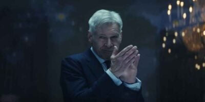 President Ross (Harrison Ford) with grey hair wearing a dark suit and tie is seen clapping in a dimly lit room. He has a serious expression on his face. In the background, there is a decorative light fixture with multiple lit bulbs, reminiscent of scenes from the MCU movies like Captain America 4.